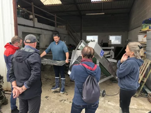 Un producteur d'huîtres faisant visiter son entreprise à Vendée, il tient une poche à huîtres dans ses mains pour expliquer son métier d'ostréiculteur aux quatre visiteurs présents sur son exploitation à Bouin.