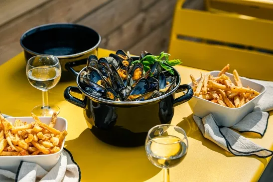 Une cocotte remplie de moules, accompagnée de deux ramequins de frite.